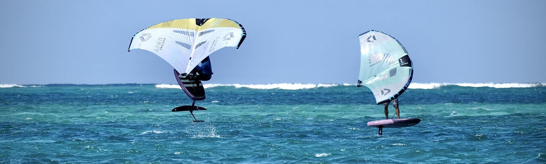 Zwei Personen betreiben Wingfoiling auf offenem Meer, mit bunten Tragflächen und Foilboards über der Wasseroberfläche.