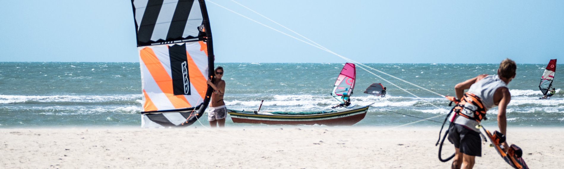 Windsurfer und Kitesurfer am sonnigen Strand von Maceio, Brasilien mit klarem Himmel.