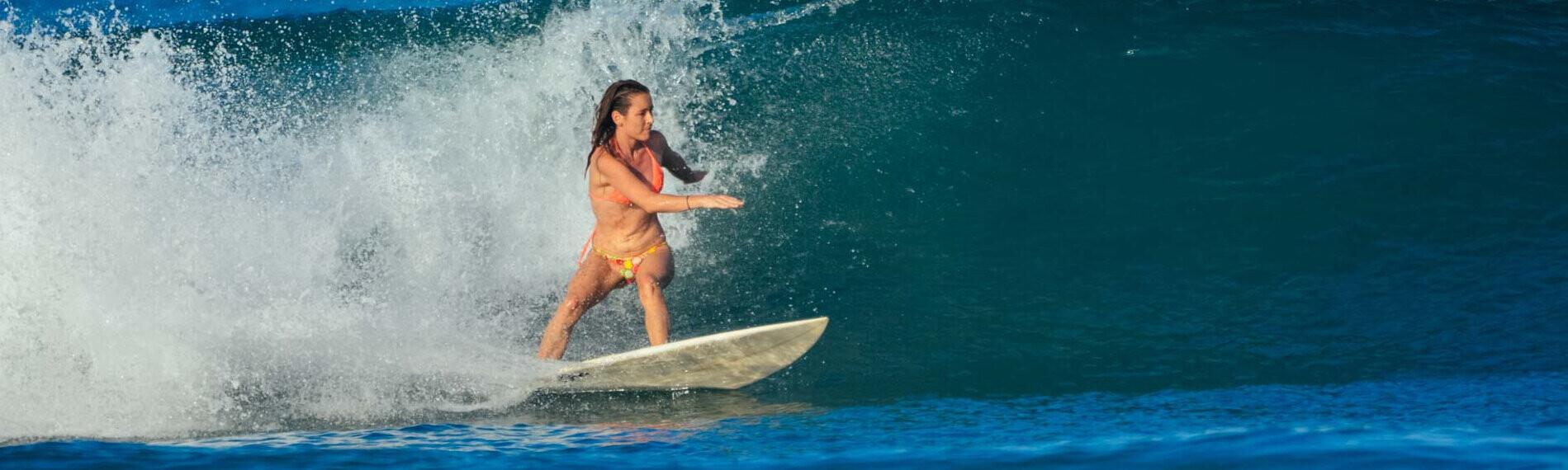 Surferin fährt eine Welle im blauen Meer entlang, dynamische Pose und spritzendes Wasser.