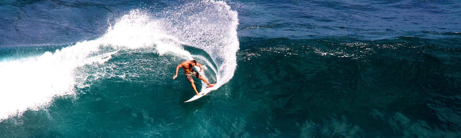 Ein Surfer navigiert dynamisch auf einer großen Welle im offenen Meer unter strahlend blauem Himmel.