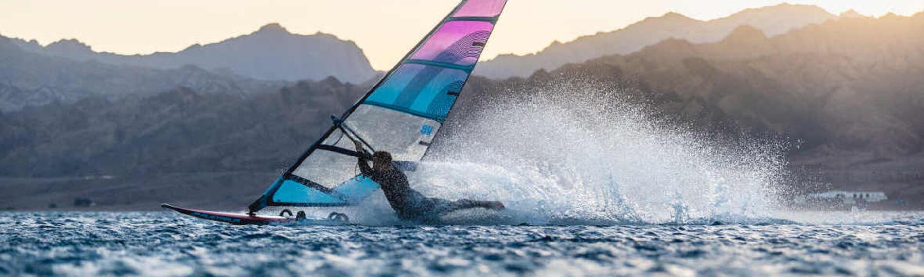 Windsurfer gleitet bei Sonnenuntergang &uuml;ber das Wasser, Berge im Hintergrund am Harry Nass Spot in Dahab Sinai.