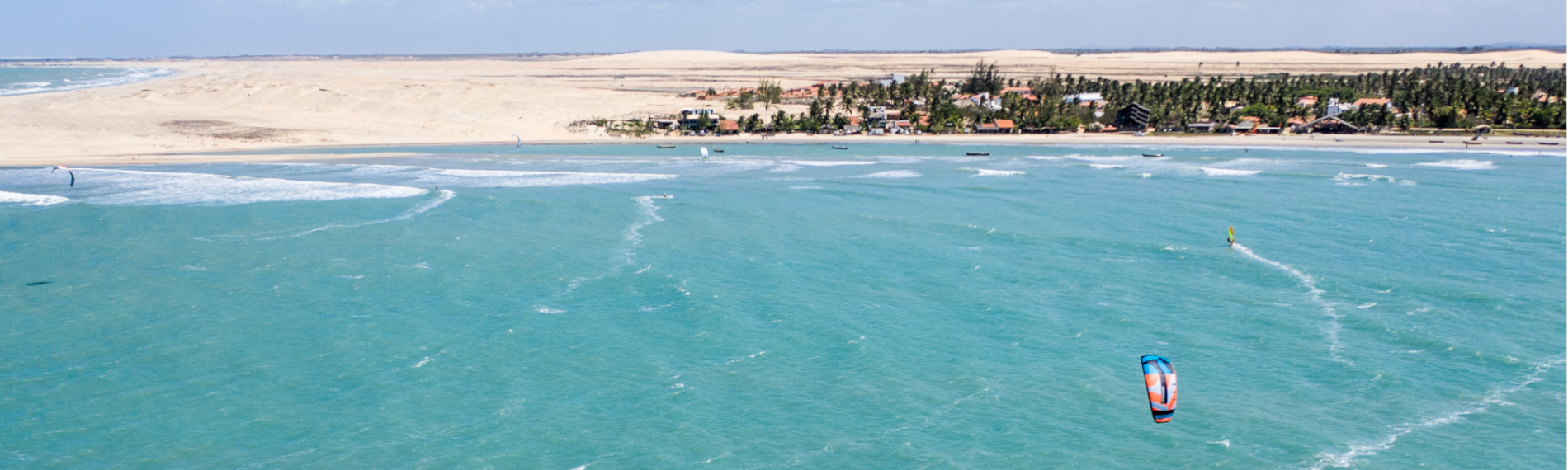 Kite-Surfer auf türkisfarbenem Meer vor sandiger Küste Maceios, Brasilien mit Vegetation.