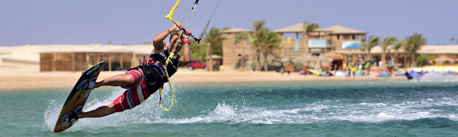 Kitesurfer springt über Wasser vor Strandkulisse in der Soma Bay