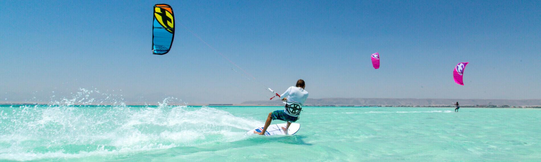 Person beim Kitesurfen in El Gouna auf türkisfarbenem Wasser mit anderen Kitesurfern im Hintergrund.